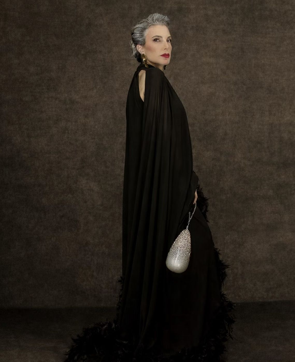 The Eternal Muse for Manar Laktineh, a woman in a black feathered cape holding a pearl bag